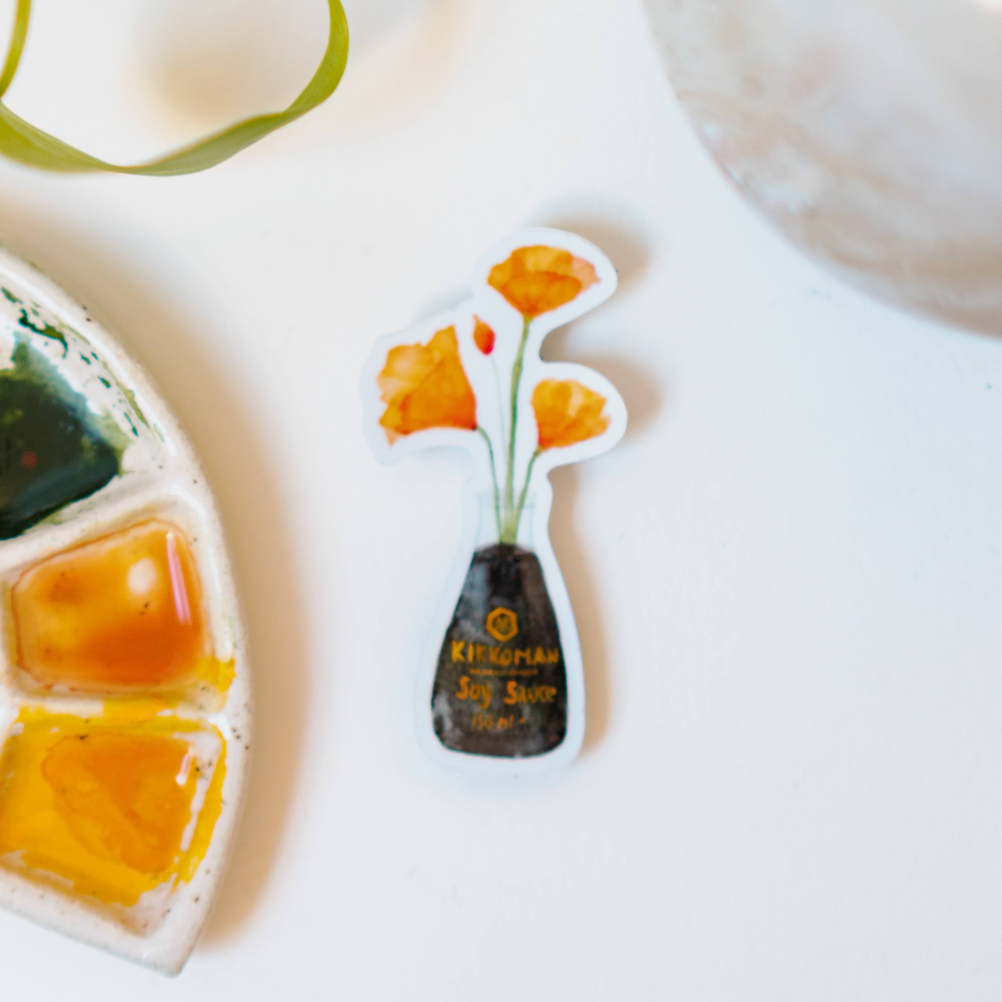 A white sticker of four orange California Poppies in a soy sauce bottle.
