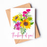 A greeting card of a cheery watercolor boquet, made of sunflowers, carnations, and other flowers. The words "thinking of you!" are written across the bottom of the card in cursive.