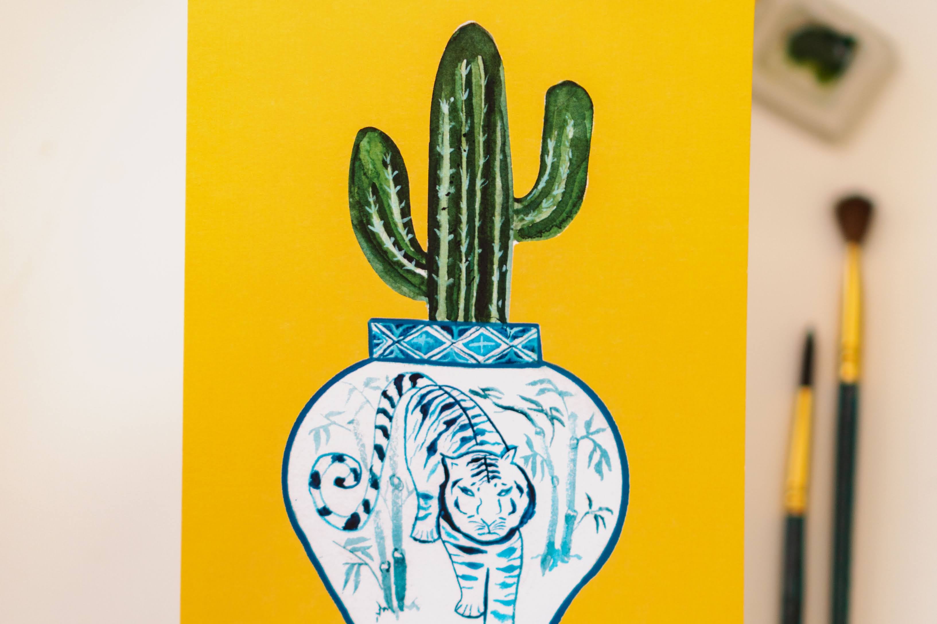 A print of a saguaro cactus in a blue and white porcelain vase, decorated with a tiger.