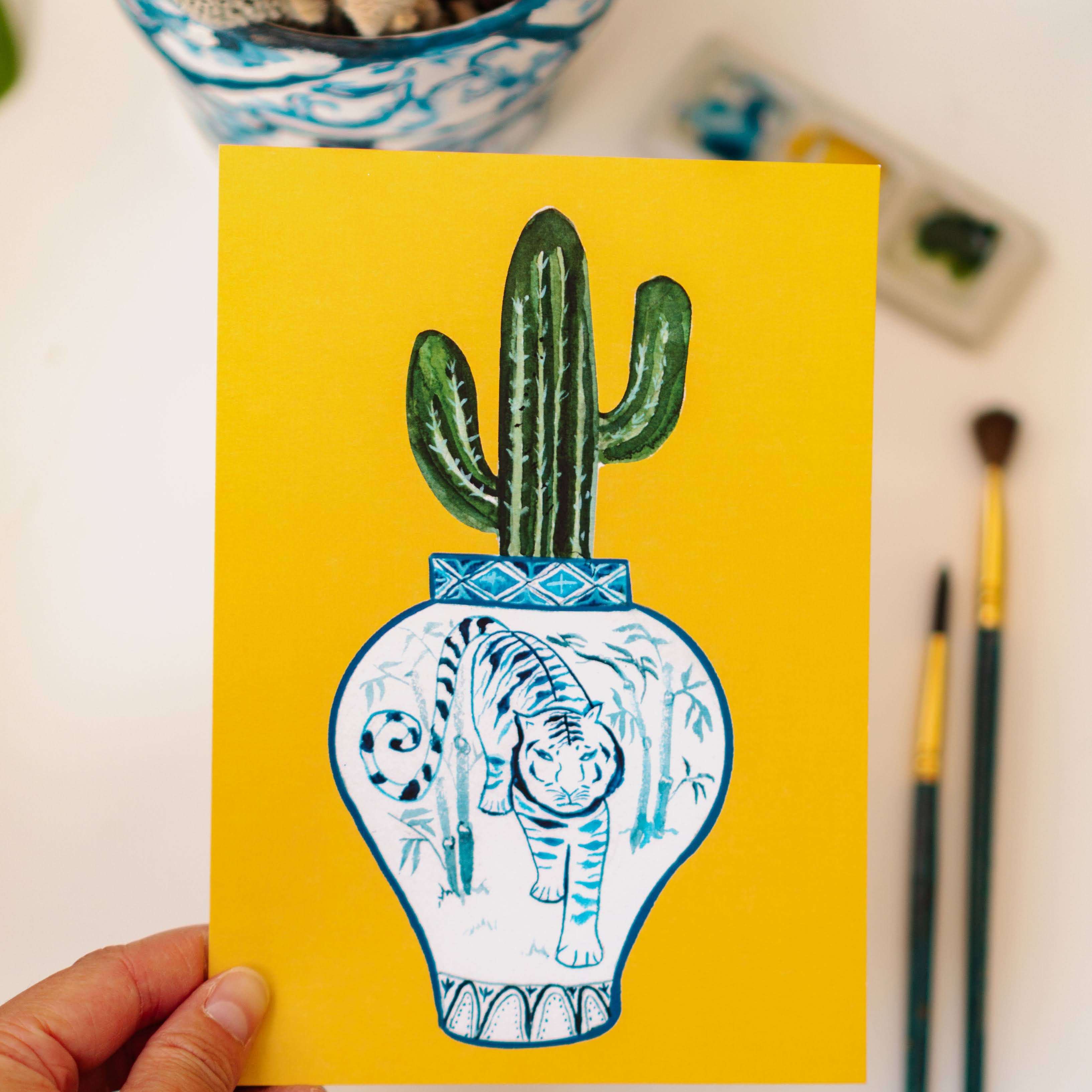 A print of a saguaro cactus in a blue and white porcelain vase, decorated with a tiger.