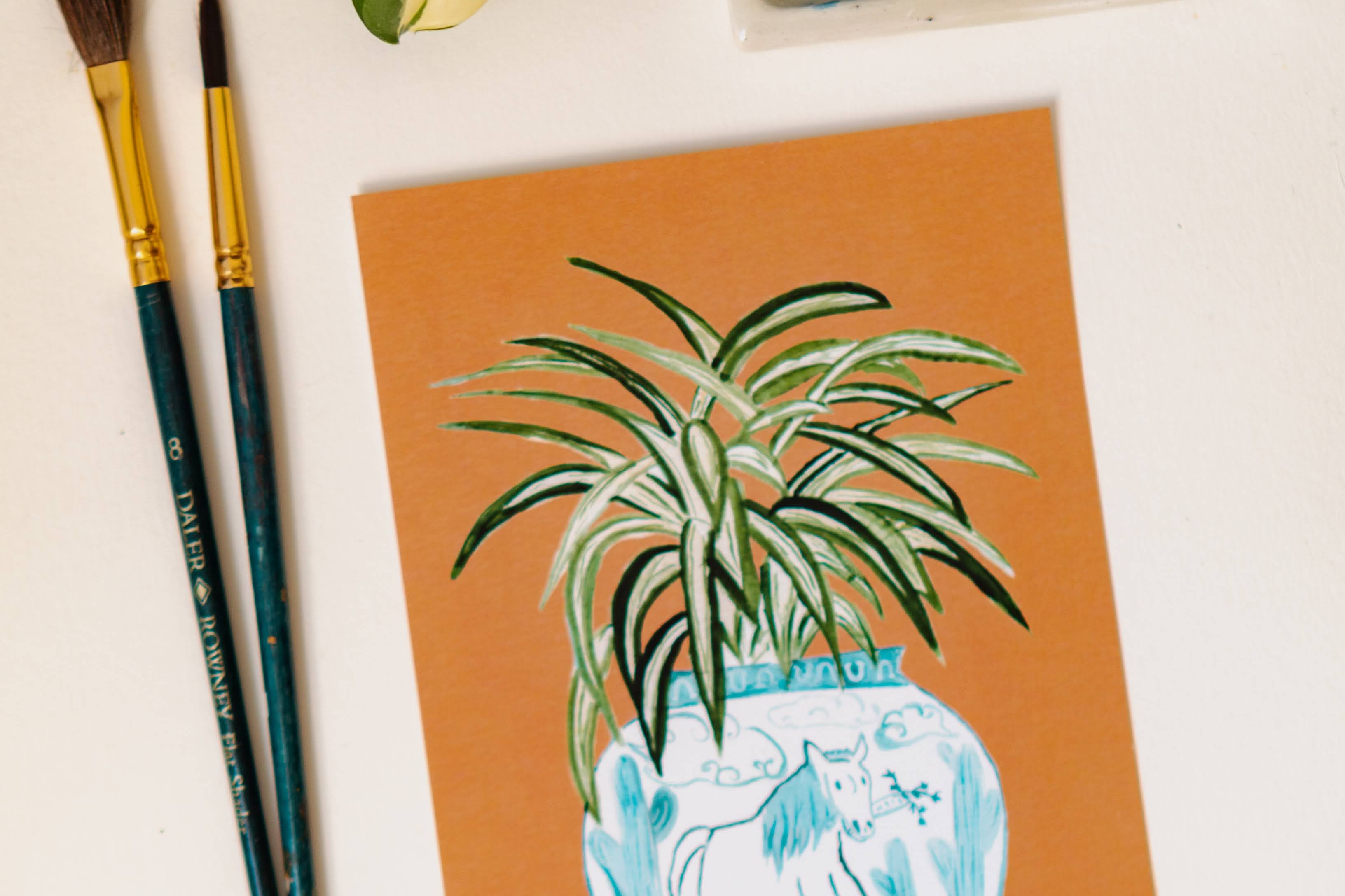 A print of a spider plant in a blue and white porcelain vase, decorated with a horse.