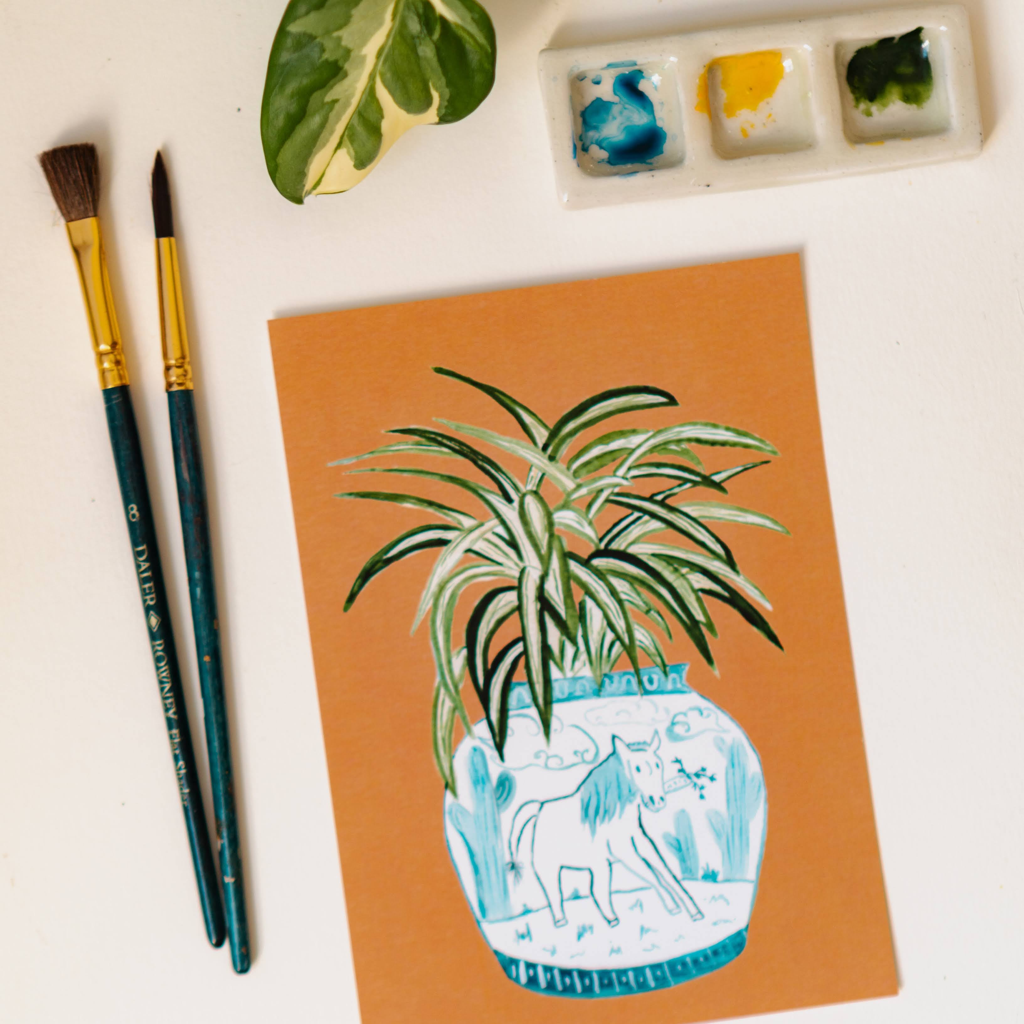 A print of a spider plant in a blue and white porcelain vase, decorated with a horse.