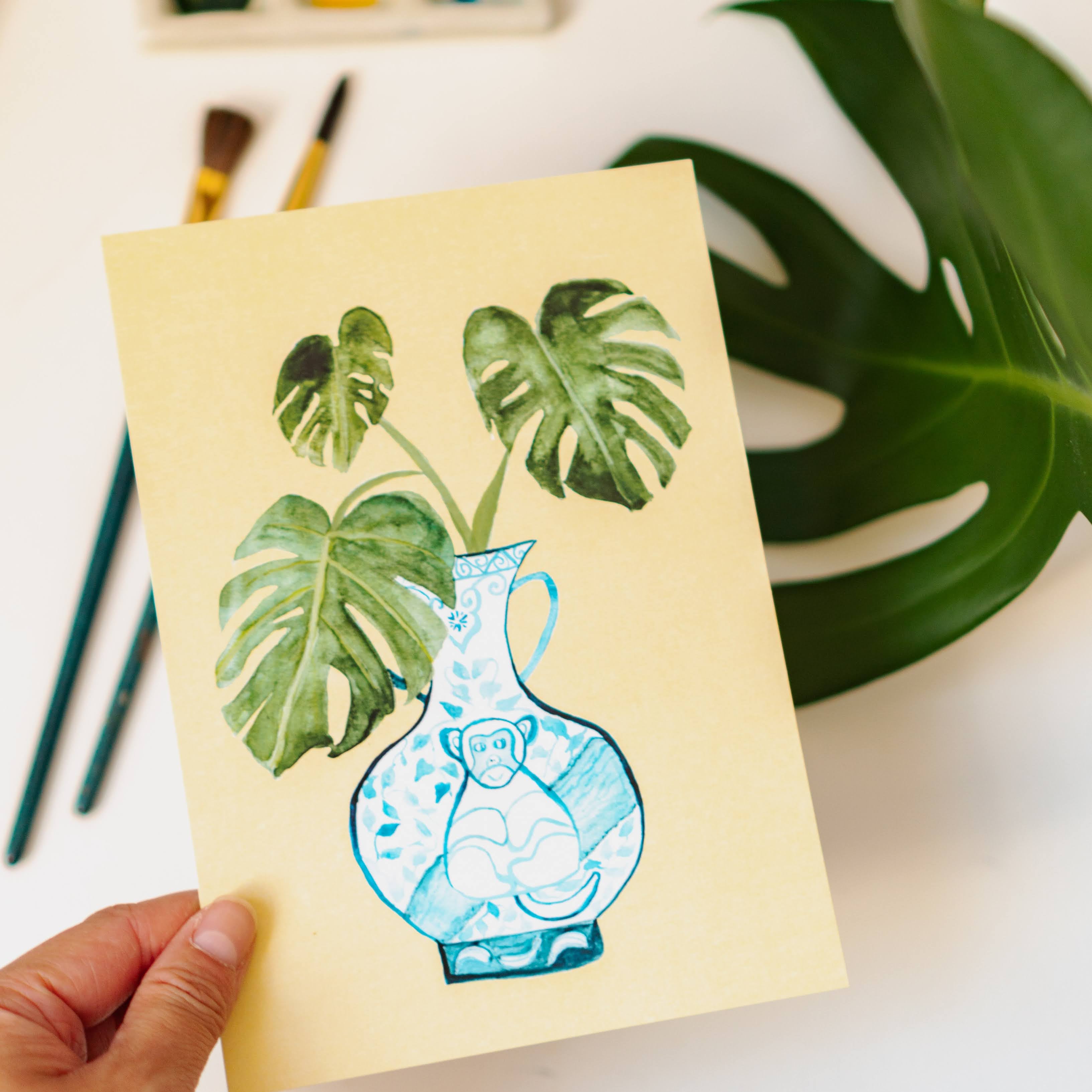 A print of a monstera plant in a blue and white porcelain vase, decorated with a monkey.