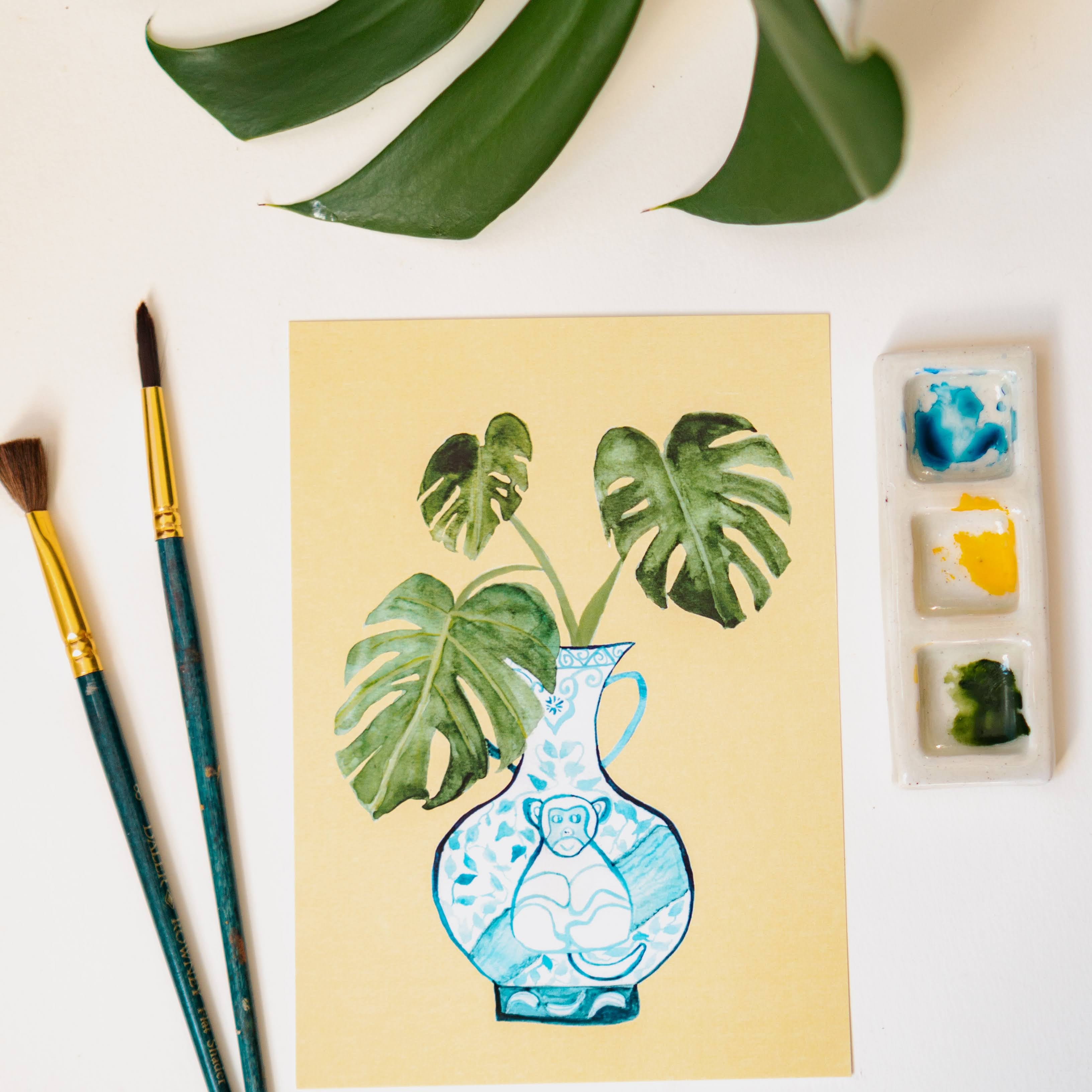 A print of a monstera plant in a blue and white porcelain vase, decorated with a monkey.