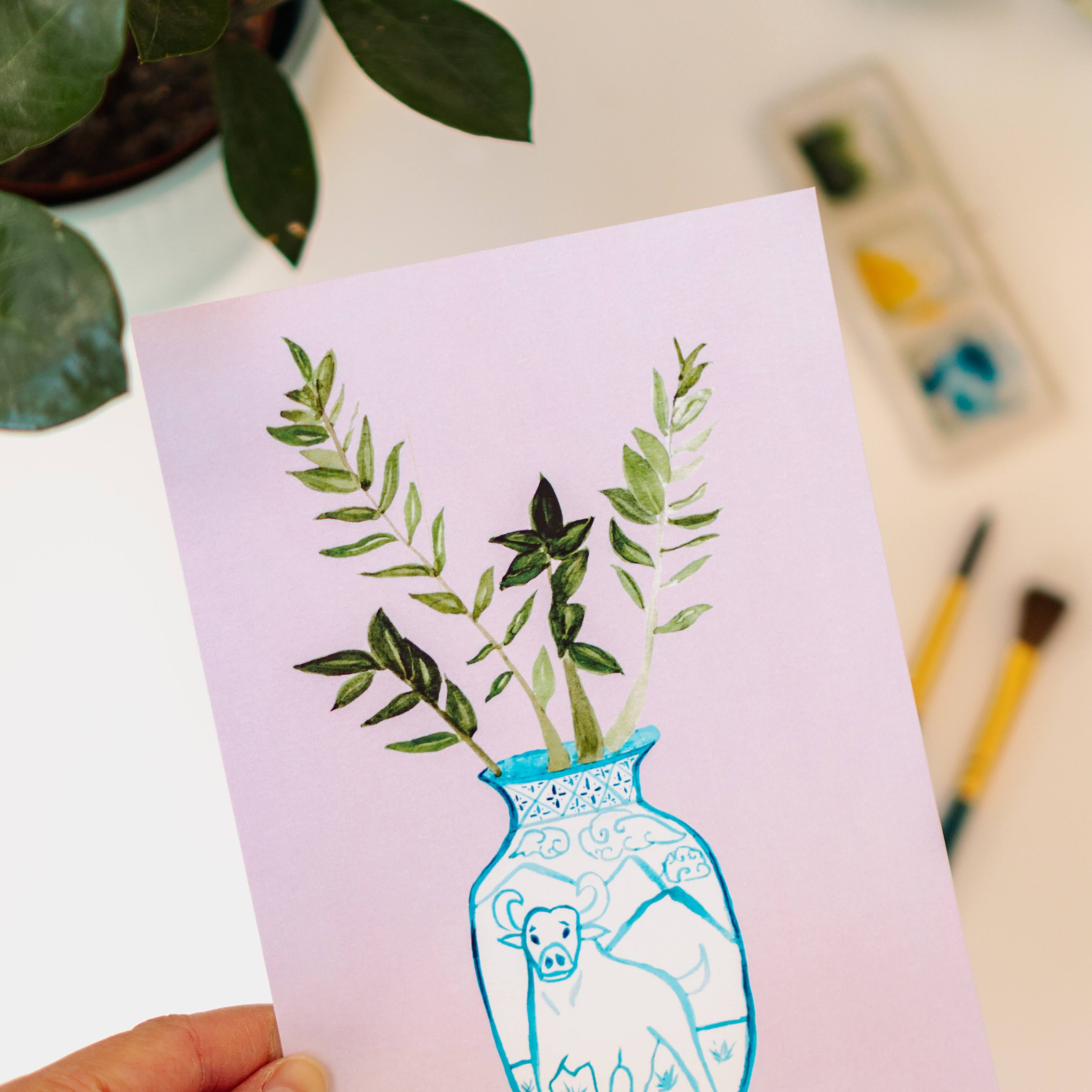 A print of a ZZ plant in a blue and white porcelain vase, decorated with an ox.
