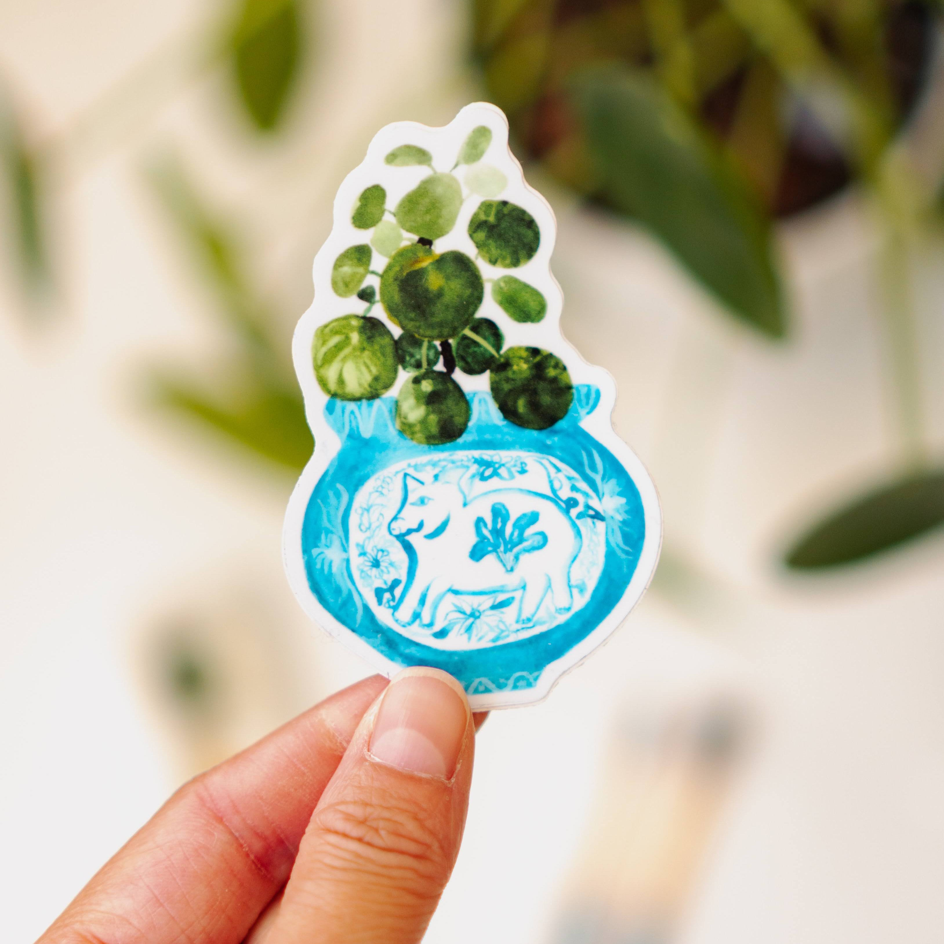 A sticker of a pilea plant in a blue and white porcelain vase, decorated with a pig.