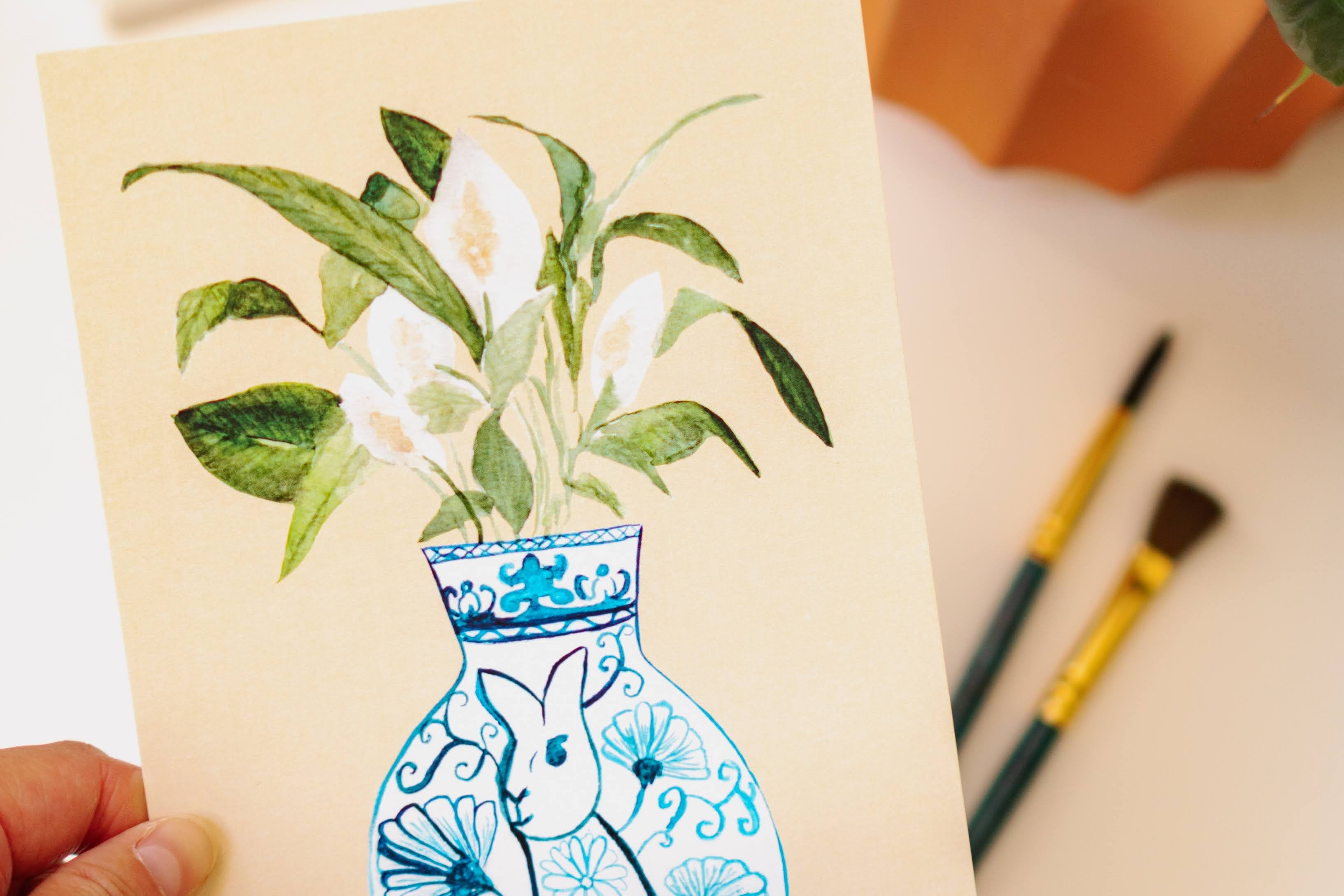 A print of a peace lily plant in a blue and white porcelain vase, decorated with a rabbit.