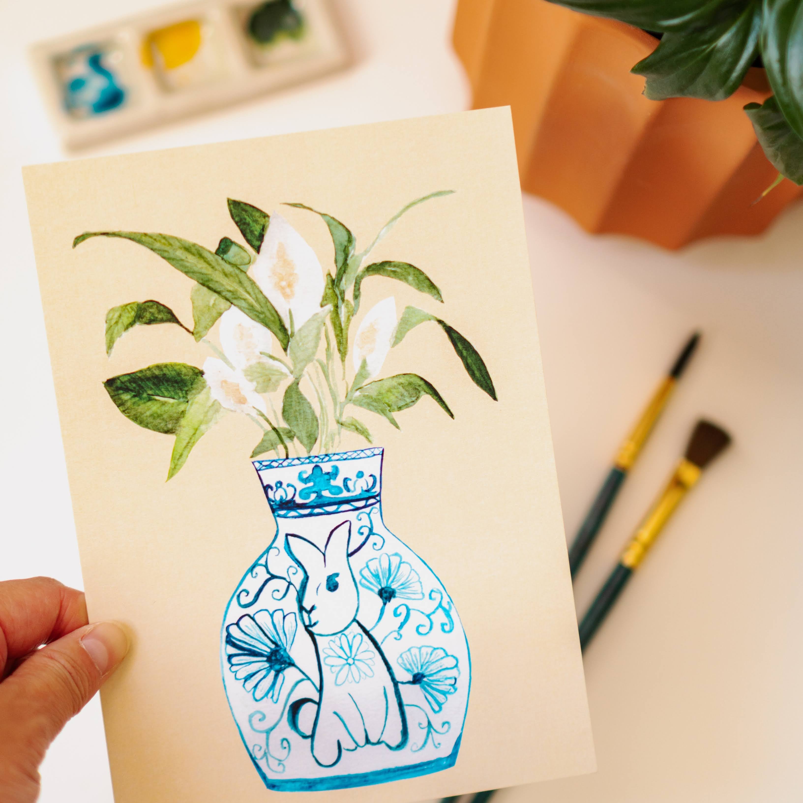 A print of a peace lily plant in a blue and white porcelain vase, decorated with a rabbit.