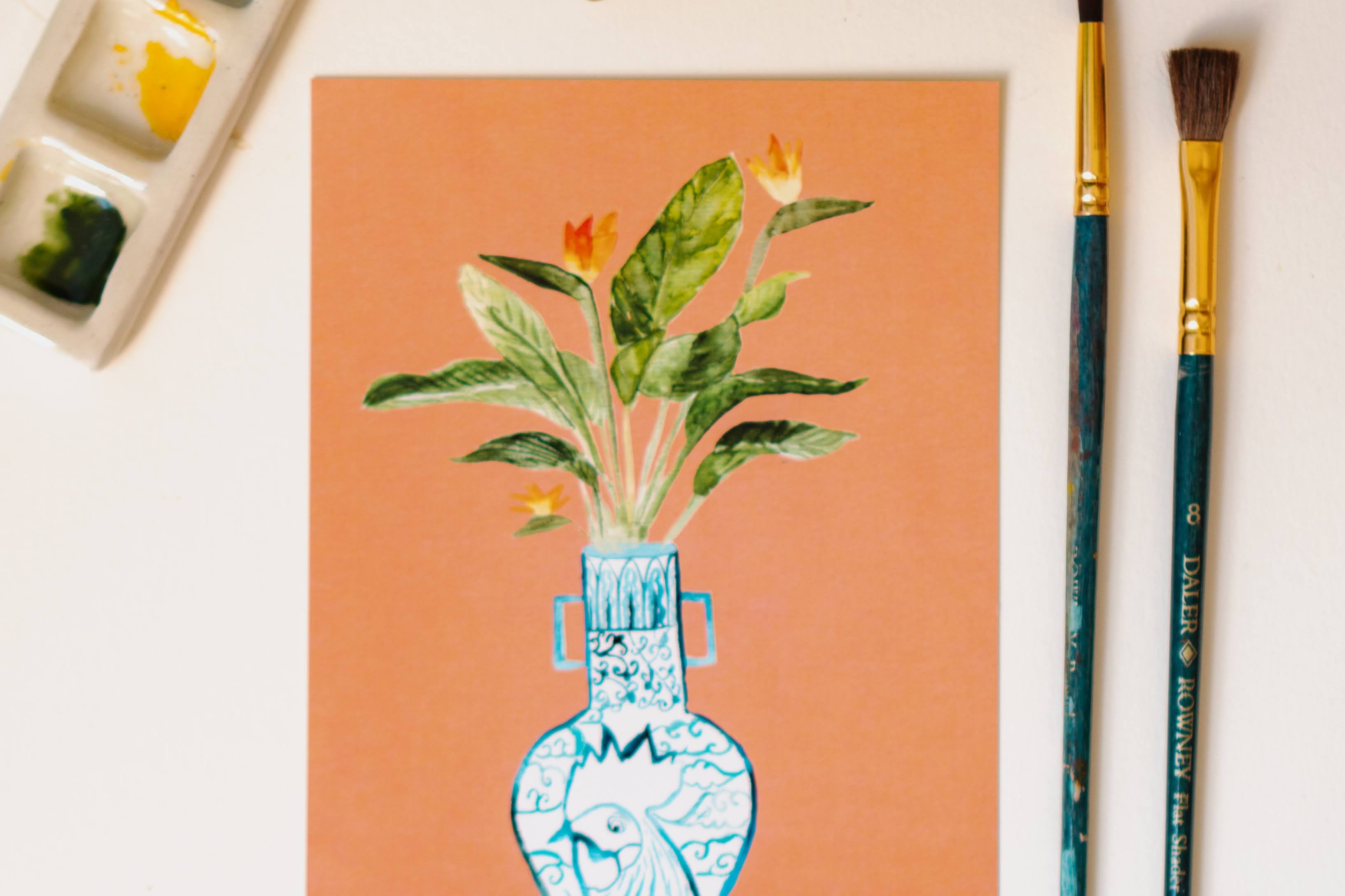 A print of a bird of paradise plant in a blue and white porcelain vase, decorated with a rooster.