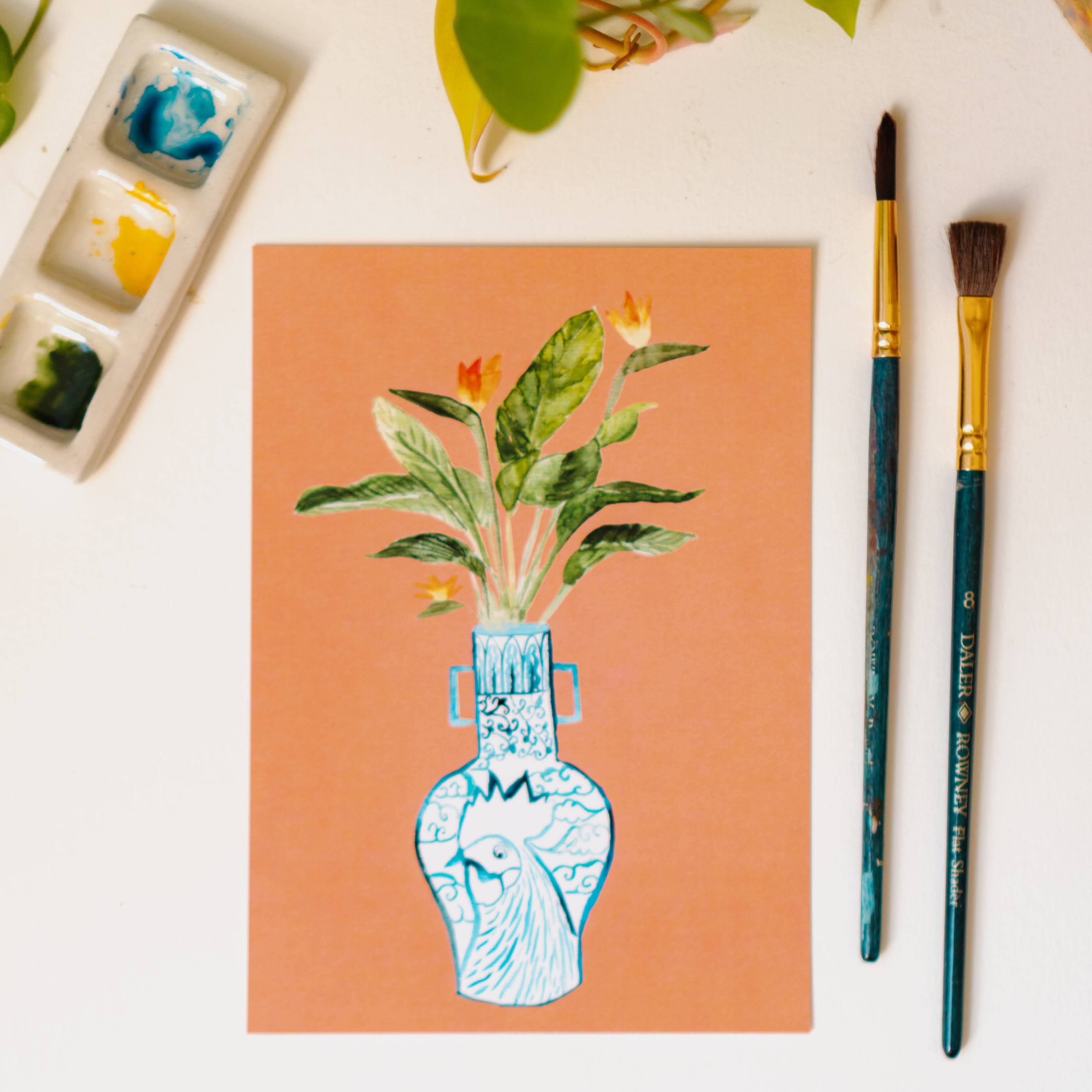 A print of a bird of paradise plant in a blue and white porcelain vase, decorated with a rooster.