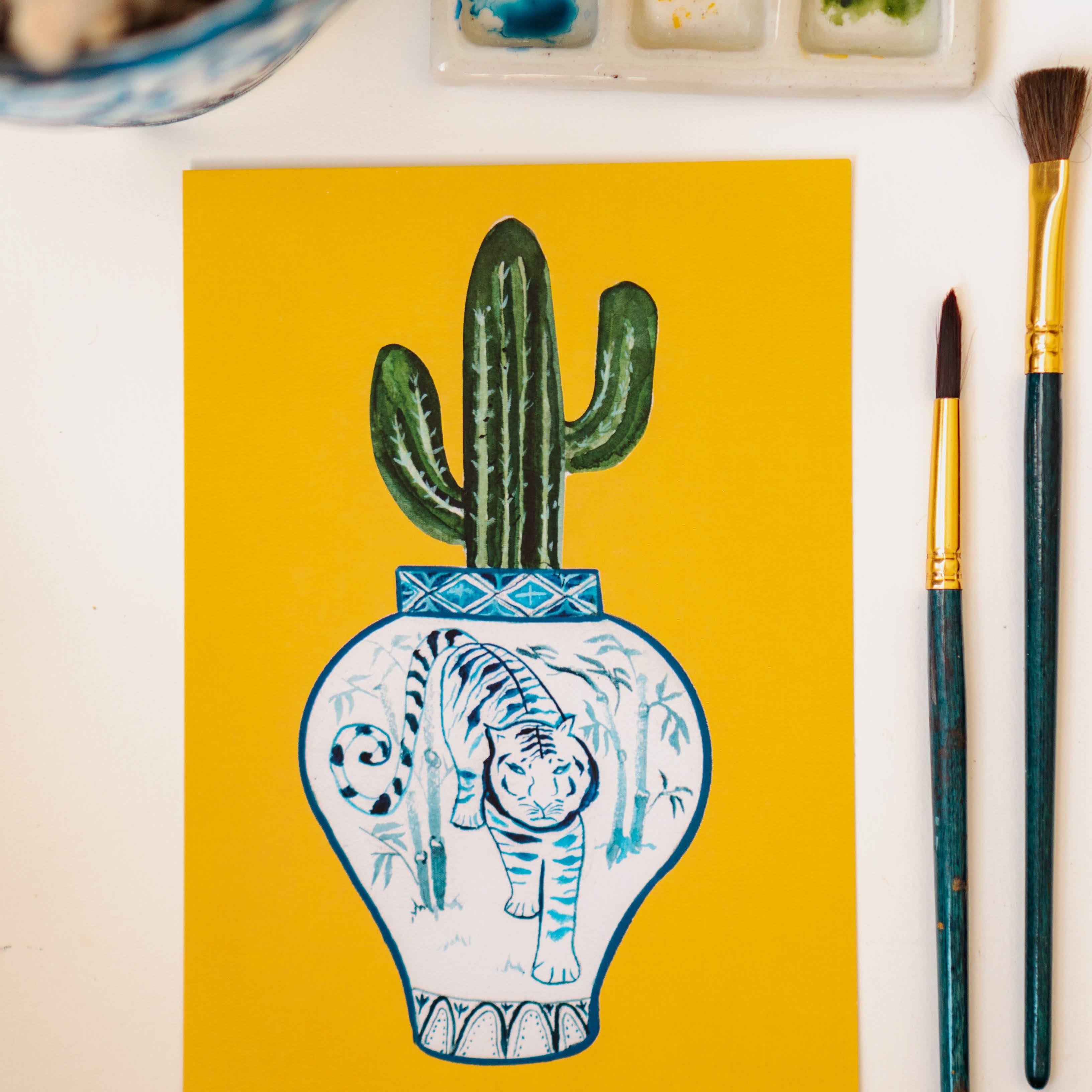A print of a saguaro cactus in a blue and white porcelain vase, decorated with a tiger.