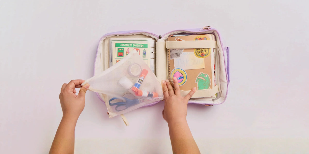 Hands opening a lavender Menmin Multi Bag filled with journals, stickers and craft supplies