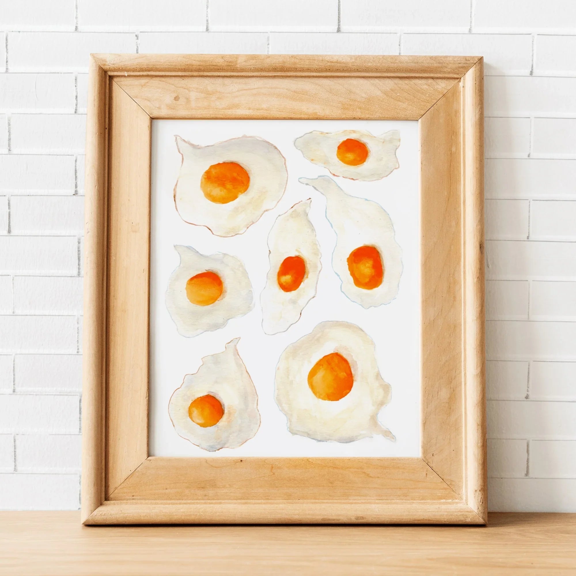 Watercolor fried egg art print in light wood frame, whimsical kitchen wall decor