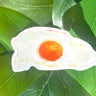 A narrow, white sticker of a fried, sunny side up egg with a rich yellow yolk and crispy edges.