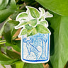 A sticker of a pothos plant in a blue and white porcelain vase, decorated with a goat.