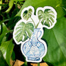 A sticker of a monstera plant in a blue and white porcelain vase, decorated with a monkey.